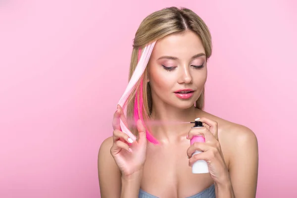 Attraktive junge Frau streicht Haarsträhne mit Spray isoliert auf rosa — Stockfoto