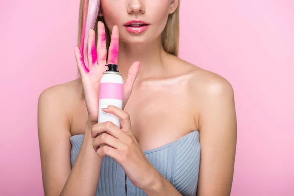 Tiro recortado de mujer joven sosteniendo pintura en aerosol para el pelo en frente de la mano cubierta con pintura rosa aislado en rosa - foto de stock