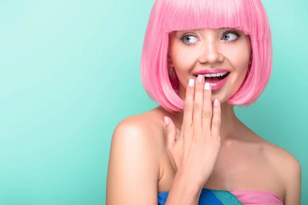 Smiling young woman with pink bob cut covering mouth with hand isolated on turquoise — Stock Photo