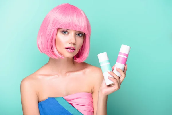 Jovem atraente com bob rosa cortar segurando latas de coloração sprays de cabelo isolado em turquesa — Fotografia de Stock