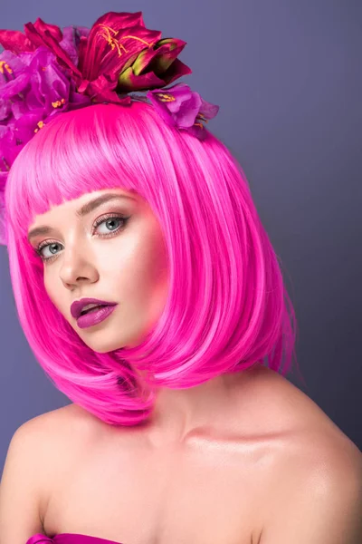 Atractiva joven con corte de color rosa bob y flores en el pelo mirando a la cámara aislada en violeta — Stock Photo
