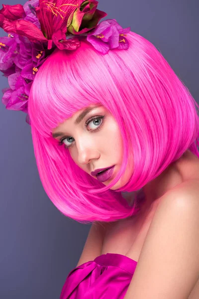 Schöne junge Frau mit rosafarbenem Bob-Schnitt und Blumen im Haar, die in die Kamera schaut, isoliert auf violett — Stockfoto