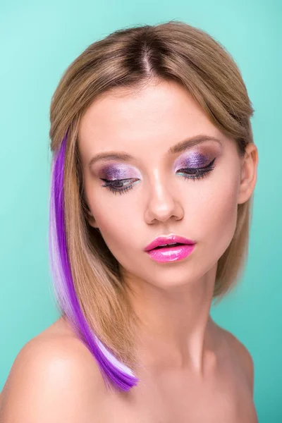 Retrato de cerca de mujer joven atractiva con maquillaje elegante y hebra de pelo púrpura aislado en azul - foto de stock