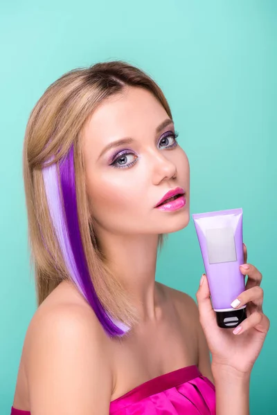 Atractiva mujer joven con cabello encorvado con hebras púrpuras y tónico para colorear el cabello mirando a la cámara aislada en azul - foto de stock