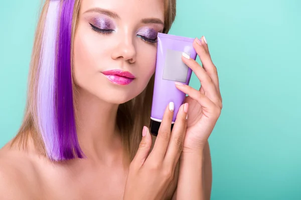 Sensual young woman with colorful hair holding hair tonic tube isolated on blue — Stock Photo