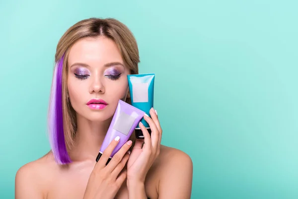 Sensual mujer joven con hebras de colores en el pelo que sostiene tónicos para el cabello colorante aislado en azul - foto de stock