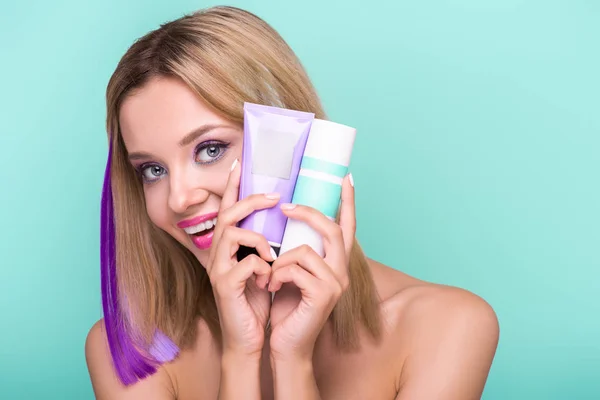 Schöne junge Frau mit bunten Strähnen im Haar mit Färbung Haarwasser Blick auf Kamera isoliert auf blau — Stockfoto