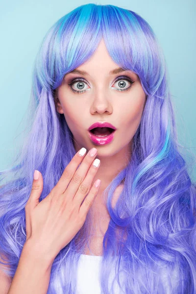 Shocked young woman covering mouth with hand and looking at camera isolated on blue — Stock Photo