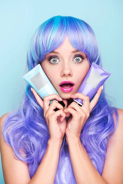 Shocked young woman with tubes of coloring hair tonics isolated on blue — Stock Photo