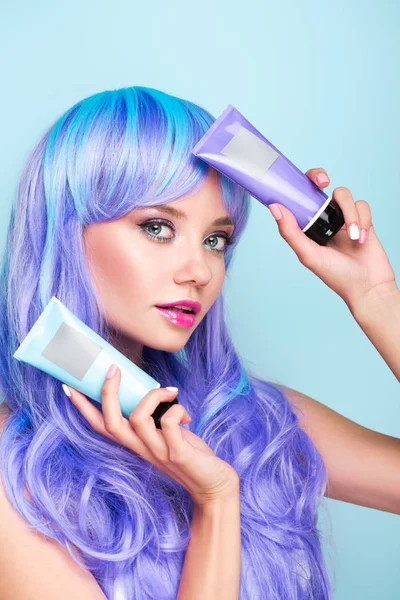 Attraente giovane donna con tubi di coloranti tonici per capelli isolati su blu — Foto stock