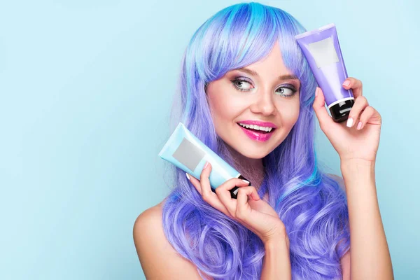 Mujer joven feliz con tubos de tónicos para colorear el cabello aislado en azul - foto de stock