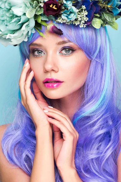 Retrato de cerca de mujer joven atractiva con pelo rizado azul y corona floral aislada en azul - foto de stock