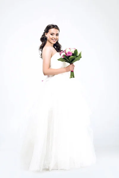 Bela noiva jovem em vestido de noiva com buquê e olhando para a câmera no branco — Fotografia de Stock