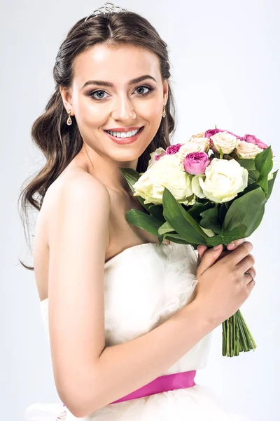 Close-up portrait of beautiful young bride in wedding dress with earrings and tiara holding bouquet isolated on white — Stock Photo