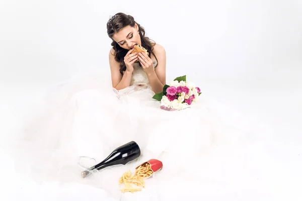 High angle view of young bride in wedding dress eating fast food while sitting on floor on white — Stock Photo