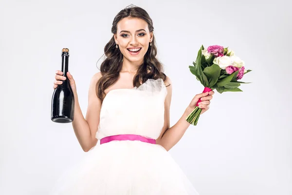 Happy young bride in wedding dress with champagne bottle and bridal bouquet isolated on white — Stock Photo