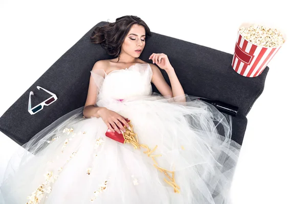 Vista de ángulo alto de la novia joven en vestido de novia durmiendo en el sofá con comida chatarra aislada en blanco - foto de stock