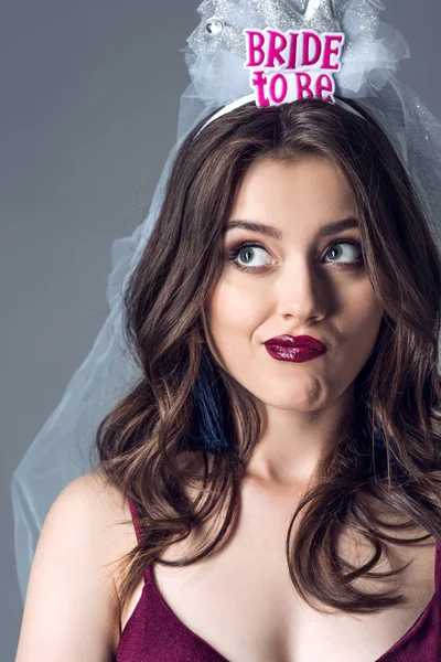 Close-up portrait of confused future bride in veil for bachelorette party looking up isolated on grey — Stock Photo