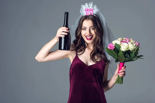 Sorridente futura sposa in velo per addio al nubilato con bouquet e champagne guardando la fotocamera isolata sul grigio — Foto stock