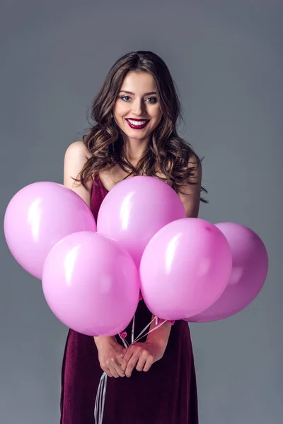 Улыбающаяся молодая женщина с кучей розовых шариков, изолированных на сером — стоковое фото