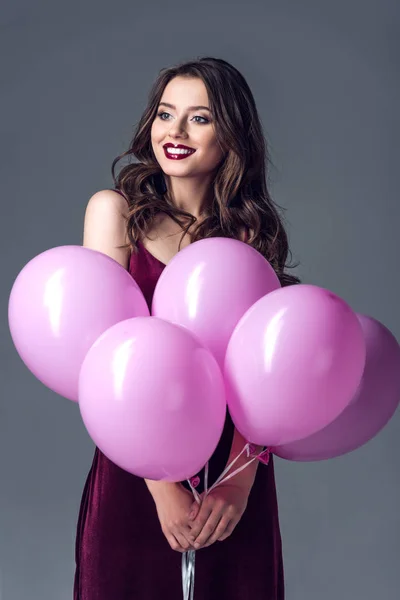 Happy young woman with bunch of pink balloons isolated on grey — Stock Photo