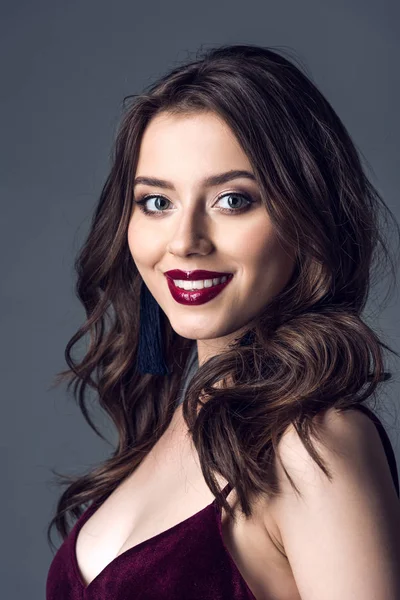 Close-up retrato de bela jovem com cabelo encaracolado e maquiagem elegante olhando para a câmera isolada em cinza — Fotografia de Stock