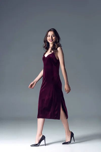 Hermosa mujer joven en vestido elegante y tacones altos caminando sobre gris — Stock Photo