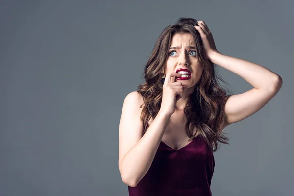 Mujer joven asustada en vestido rojo con estilo mirando hacia otro lado aislado en gris - foto de stock