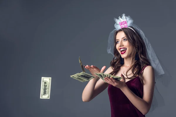 Beautiful future bride in veil for bachelorette party throwing money away isolated on grey — Stock Photo
