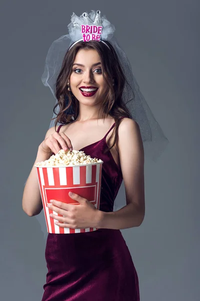 Happy future bride in veil for bachelorette party isolated with popcorn bucket on grey — Stock Photo
