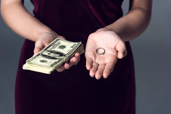 Cropped shot of woman holding stack of cash and wedding ring, marriage of convenience concept — Stock Photo