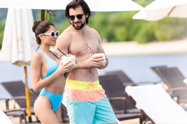 Young couple with coconut cocktails standing near swimming pool — Stock Photo