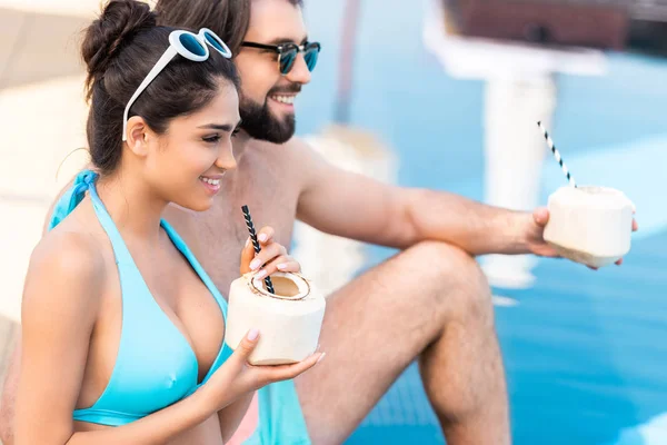 Happy couple in sunglasses with fresh coconut cocktails relaxing at swimming pool — Stock Photo