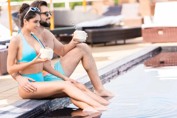 Красивая молодая пара со свежими кокосовыми коктейлями расслабляющая в бассейне — стоковое фото