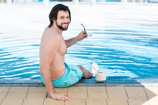 Homme barbu avec cocktail de noix de coco verte assis à la piscine — Photo de stock