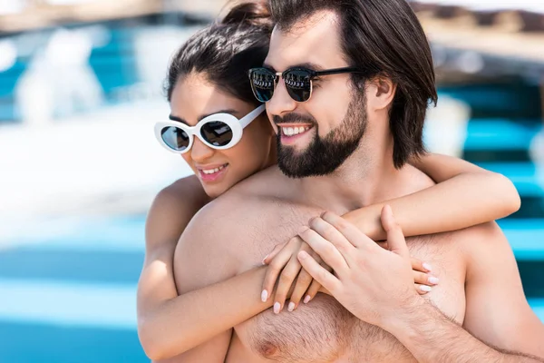 Couple souriant dans des lunettes de soleil embrassant près de la piscine — Photo de stock