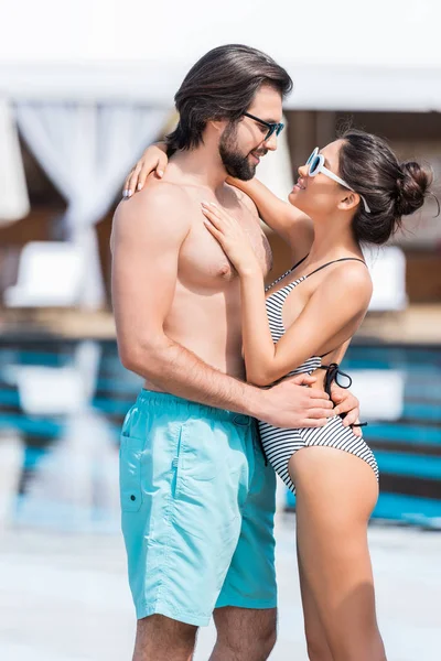 Красива пара в сонцезахисних окулярах, що обіймаються біля басейну — стокове фото