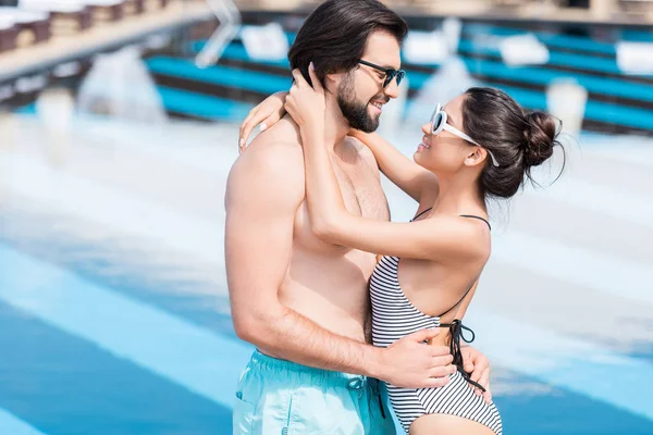 Junges Paar mit Sonnenbrille umarmt sich in Schwimmbadnähe — Stockfoto