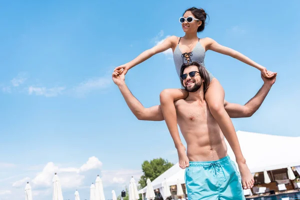 Happy girl in swimsuit having fun and sitting on shoulders of her boyfriend — Stock Photo