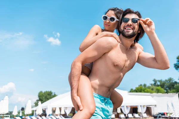 Handsome boyfriend piggybacking his girlfriend on resort — Stock Photo