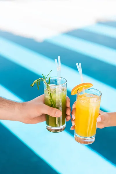 Vue partielle du couple tenant des verres avec des cocktails alcoolisés à la piscine — Photo de stock