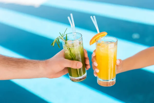 Vista recortada de la pareja sosteniendo vasos con limonadas frescas en la piscina - foto de stock