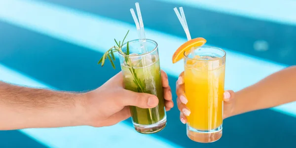 Vista recortada de la pareja sosteniendo vasos con bebidas alcohólicas en la piscina - foto de stock