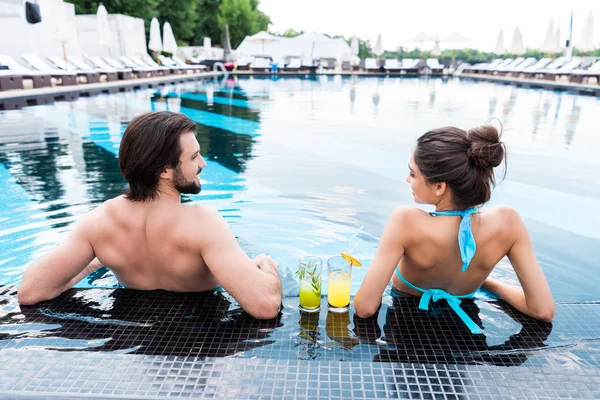 Rückansicht eines Paares mit Cocktails, die sich im Schwimmbad entspannen — Stockfoto