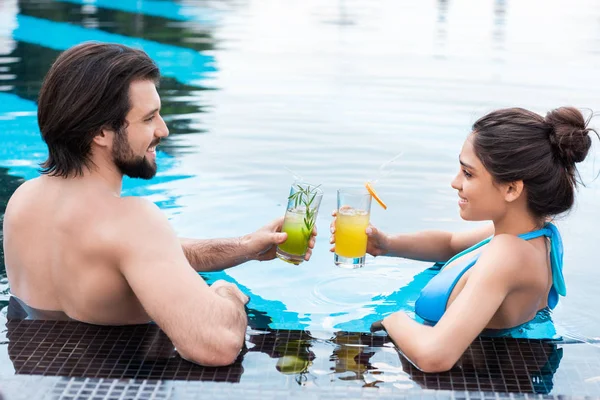 Beautiful couple clinking with cocktails and relaxing in swimming pool — Stock Photo