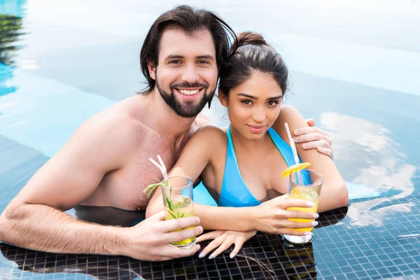 Jeune couple avec cocktails frais câlins dans la piscine — Photo de stock