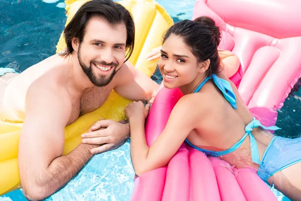 Jovem casal nadando no colchão inflável amarelo e rosa na piscina — Fotografia de Stock