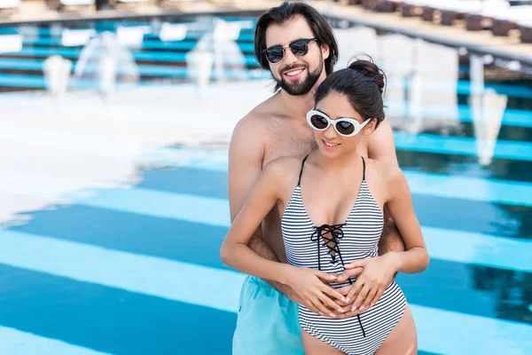 Beautiful couple in sunglasses hugging near swimming pool — Stock Photo