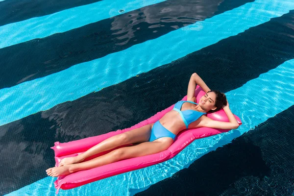 Junge Frau im Bikini liegt auf rosa aufblasbarer Matratze im Schwimmbad — Stockfoto