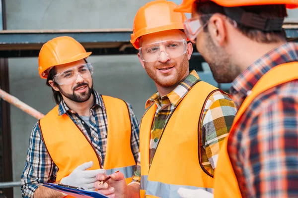 Group of builders in hard hats and reflective vests discussing work — Stock Photo